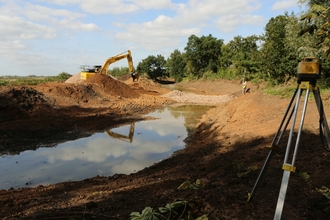A new river channel is dug by a digger with a measurement tool set up surveying the work