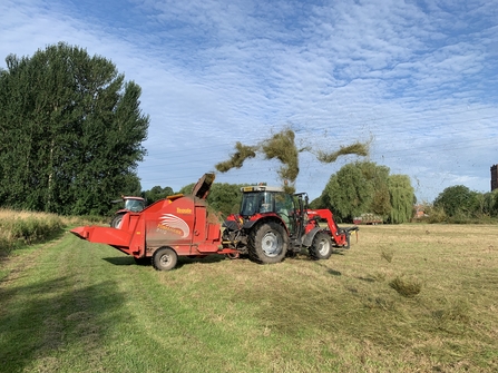 Red tractor spreading green hay at Burton washlands in summer