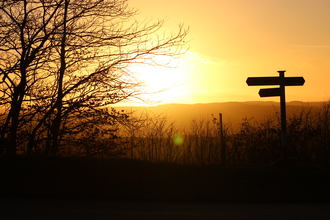 A landscape with a signpost, with a sunset in the background