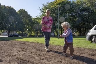 A woman and child plant wildflower seeds on a bare patch of soil in a community greenspace