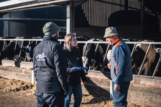 Two staff from Staffordshire Wildlife Trust talking to a farmer (man) in front of a cow shed