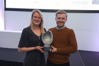 A blonde woman and a blonde man with a trophy both smiling