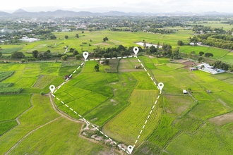 A patchwork of agricultural fields with some trees and buildings in the distance. A white dashed line indicates an outline around a plot/area.