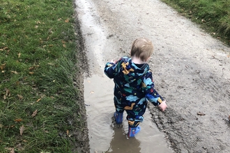 A little boy dressed for rainy weather splashes in a puddle