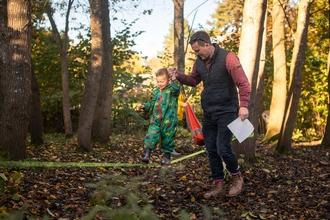 A man holds a child's hand as they walk across a slack line between two trees
