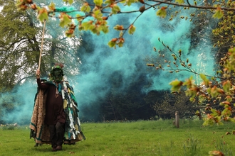 A man dressed in ceremonial garb emerges from a woodland