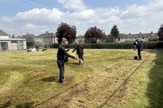 A group of people sow seeds on a former tennis court