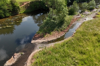 A aerial view of a river with a freshly dug channel and surrounding flora