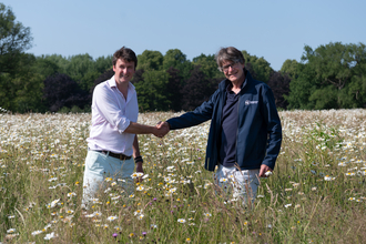 Charlie Giffard, owner of Chillington Hall shaking hands with Julian Woolford, Chief Executive of Staffordshire Wildlife Trust shaking hands and facing the camera, standing in a field full of daisies