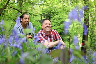 A man and woman knelt down amongst bluebells in the woods.