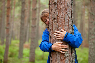 A woman in a blue jacket hugging a pine tree.