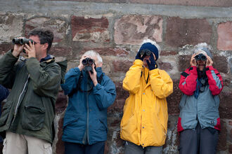 4 people facing the camera with binoculars, all wearing different coloured anoraks.