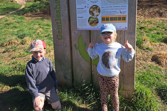 Two children on a nature reserve, wearing caps and sunglasses.