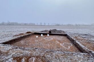 A square dig site sits on a frozen field.