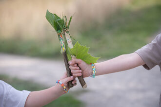 Two wands made from tree sticks and leaves held together by two children (out of shot)