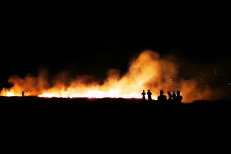 A silhouette of a group of people standing in front of a fire at night time.