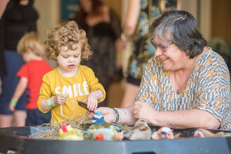 A woman and a child with a yellow shirt on playing with natural crafts.