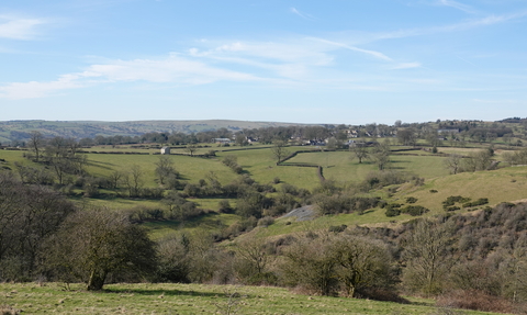 An expanse of farm land and wood pasture with scrub under a blue sky