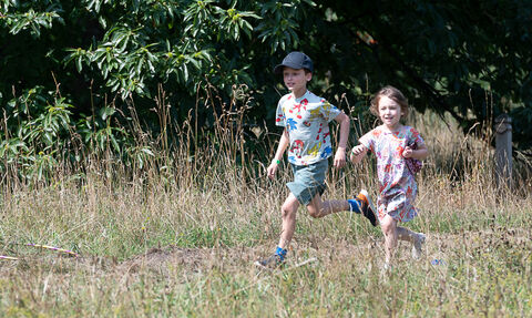 A boy and girl run through a grassy meadow looking happy