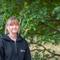 A woman with blonde hair tied in a pony tail stands in front of a tree smiling. She wears a black hooded top with Staffordshire Wildlife Trust's logo on it.