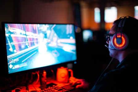 A person sat wearing headphones, gaming on a PC monitor