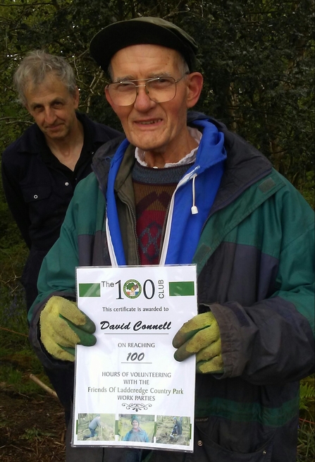 A man holds a printed award for volunteering 100 hours