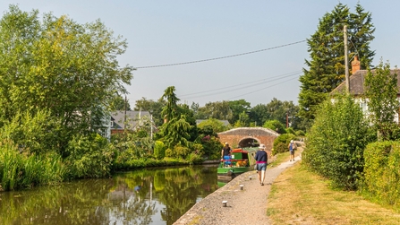 A canal with a barge and people walking down a path.