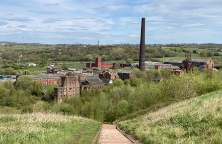 A colliery and buildings in the distance beyond a grassy hill