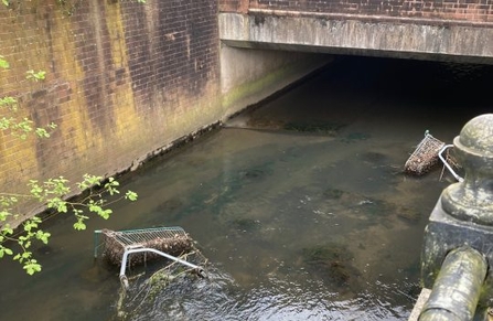 A shopping trolly abandoned in a brook lined with bricks