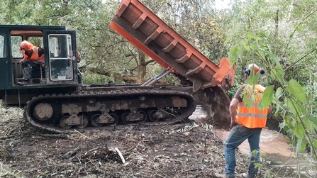 Contractors deposit gravel in a brook using large machinery