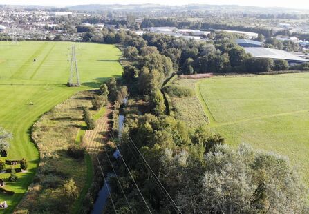 A small brook which runs straight through a landscape toward an industrial estate.