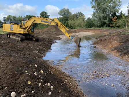A digger brining pebbles into a river to make a riffle.
