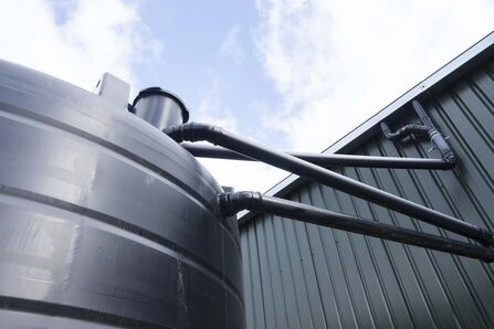 A series of pipes connect a farm building roof to a water storage system.