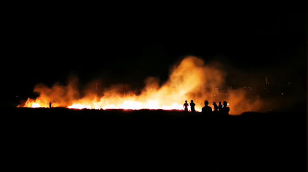 A silhouette of a group of people standing in front of a fire at night time.