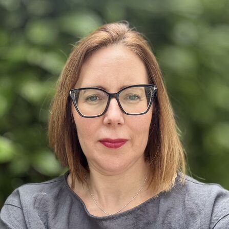 A portrait of a woman with brown hair, black glasses, and red lipstick .