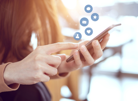 A girl holding a phone, with social media icons floating out of it.