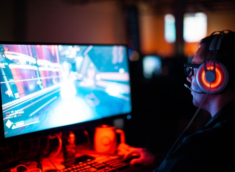 A person sat wearing headphones, gaming on a PC monitor