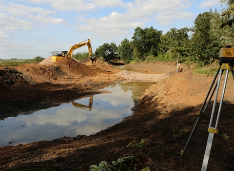 A new river channel is dug by a digger with a measurement tool set up surveying the work