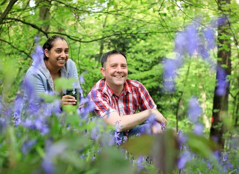 A man and woman knelt down amongst bluebells in the woods.