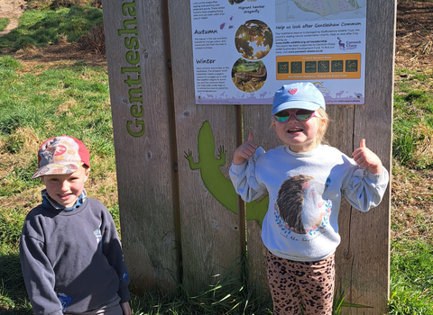 Two children wearing caps and sunglasses on a nature reserve, facing the camera and smiling.