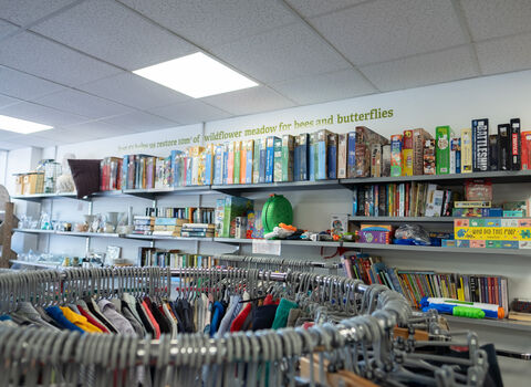 Inside a charity shop. Racks of clothes and shelves with items like puzzles, books and toys.