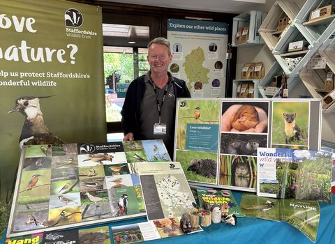 A man stands smiling at a stand filled with posters and images with wildlife information