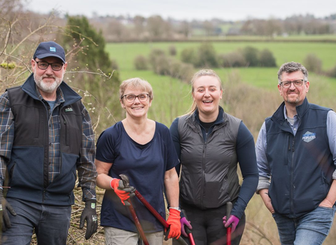 Four people on a nature reserve looking to camera, with tools.