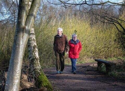 A woman in a red coat and a man in a brown jacket walking through a nature reserve in winter.