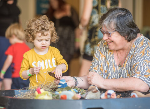 A woman and a child with a yellow shirt on playing with natural crafts.