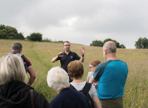 A man in a black polo shirt speaking to a group of people at a nature reserve.